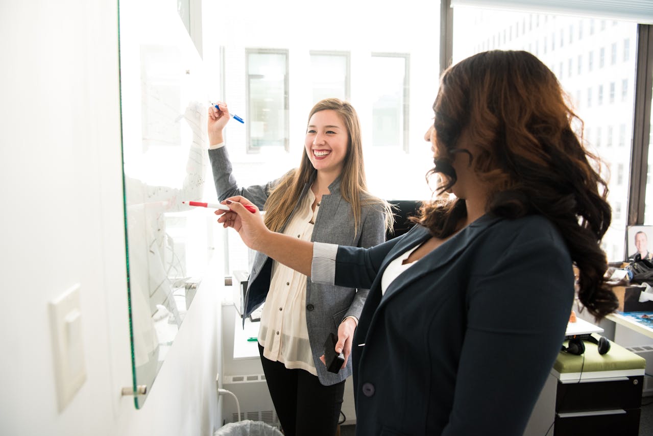 two coworkers laughing and writing on a whiteboard in the office